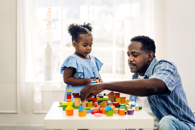 Retrato de amor feliz familia negra padre afroamericano con niñita actividad sonriente aprender y entrenar el cerebro jugar con juguetes construir bloques de madera tablero juego educativo en casadía del padre