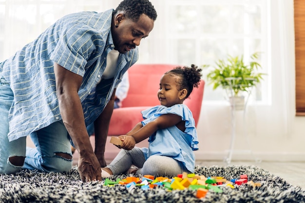 Retrato de amor feliz familia negra padre afroamericano con niñita actividad sonriente aprender y entrenar el cerebro jugar con juguetes construir bloques de madera tablero juego educativo en casadía del padre