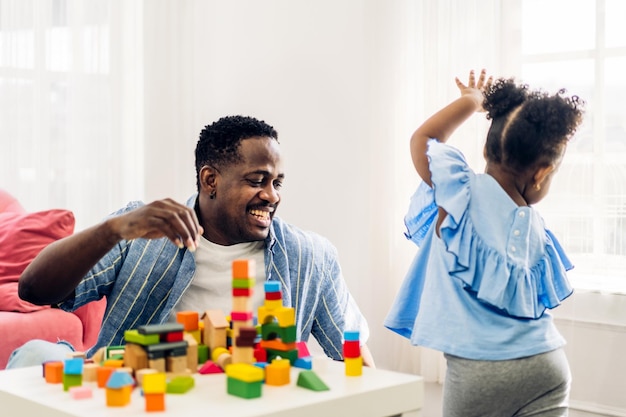 Retrato de amor feliz familia negra padre afroamericano con niñita actividad sonriente aprender y entrenar el cerebro jugar con juguetes construir bloques de madera tablero juego educativo en casadía del padre