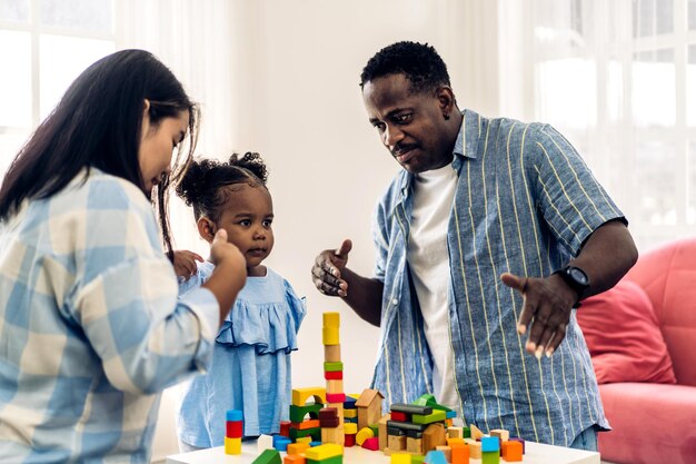 Retrato de amor feliz familia negra padre y madre afroamericanos con niñita actividad sonriente aprender y entrenar el cerebro jugar con juguetes construir bloques de madera tablero juego educativo en casa