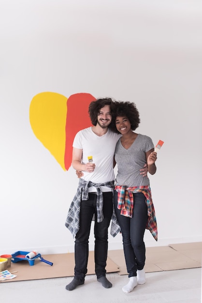 Retrato de amorosa pareja multiétnica con corazón pintado en la pared