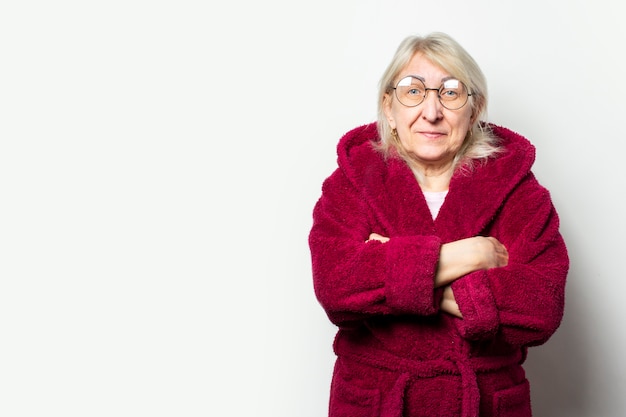 Retrato de una anciana amigable en una bata casual y gafas con los brazos cruzados sobre su pecho en una pared de luz aislada. cara emocional