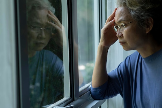 Retrato de una anciana asiática triste y preocupada mirando por la ventana en casa