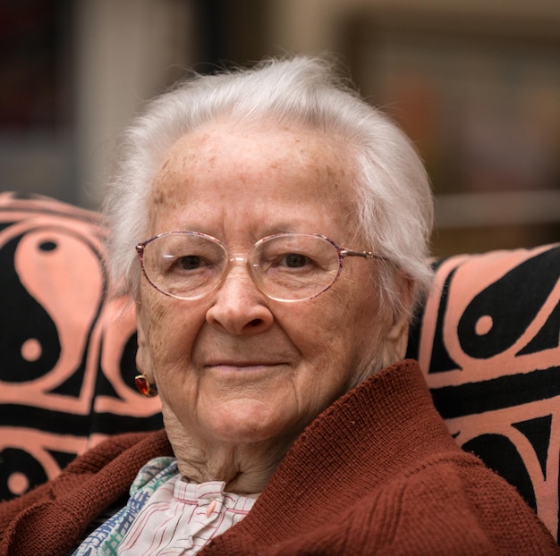 Retrato de una anciana canosa sonriente con gafas posando en casa