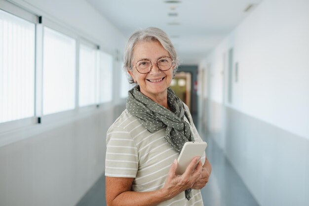 Retrato de una anciana caucásica feliz caminando por un pasillo dentro de un edificio sosteniendo un teléfono