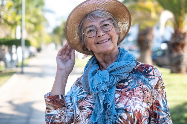 Retrato de una anciana caucásica sonriente con sombrero y anteojos al aire libre en un parque público mirando a la cámara anciana relajada disfrutando de la libertad y la jubilación
