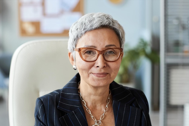 Retrato de una anciana como jefa sentada en el lugar de trabajo y sonriendo a la cámara