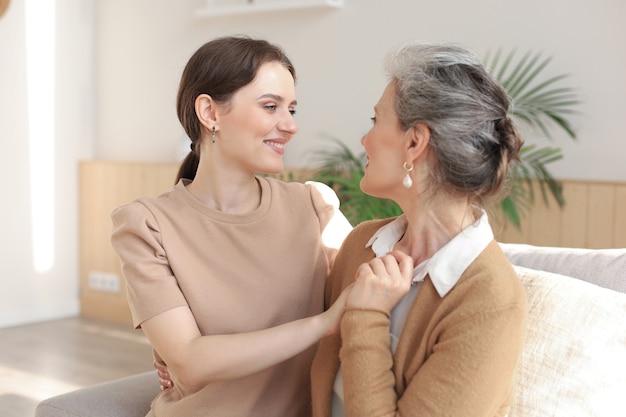 Retrato de anciana e hija madura abrazándose en casa. Feliz madre senior e hija adulta abrazándose con amor en el sofá.