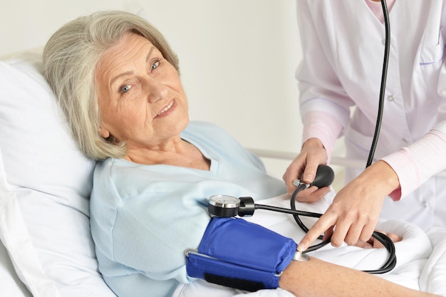 Retrato de una anciana en el hospital con un médico cariñoso midiendo la presión