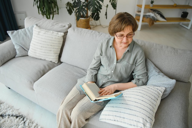 Retrato de una anciana relajada sentada en un sofá con un libro