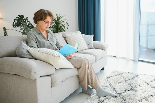 Retrato de una anciana relajada sentada en un sofá con un libro
