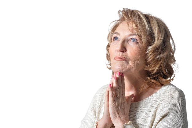 Retrato de anciana rezando con los brazos cruzados sobre fondo blanco.