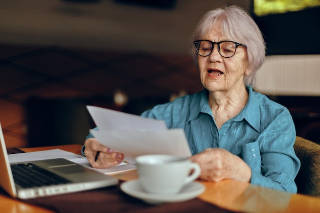 Retrato de una anciana sentada en un café con una taza de café y una computadora portátil Freelancer funciona sin cambios