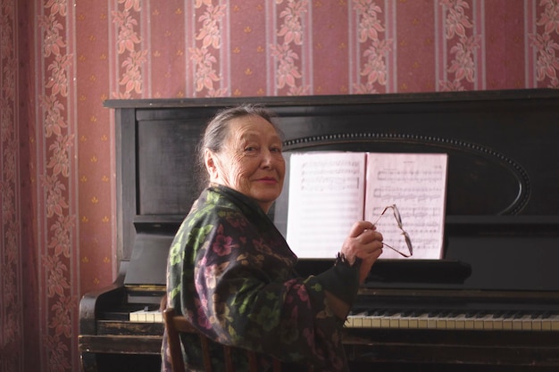 Retrato de anciana sentada frente a un piano con sus gafas en las manos, envejecimiento activo