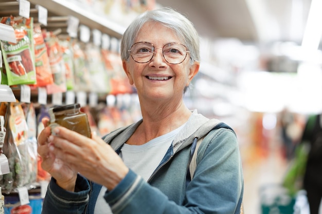 Retrato de una anciana sonriente haciendo compras en el supermercado seleccionando un poco de mermelada de clientes ancianos caucásicos en la tienda de comestibles