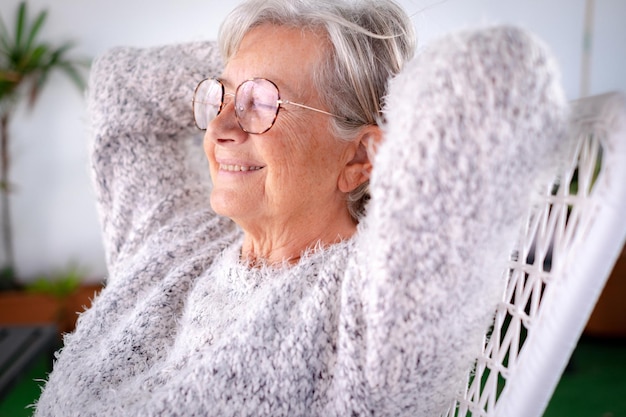 Retrato de una anciana con una sonrisa relajándose en el sillón en el balcón de casa con los ojos cerrados