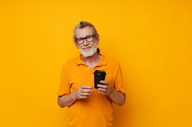 Retrato anciano en una camiseta amarilla un vaso con una bebida de fondo amarillo