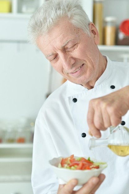Retrato de anciano chef masculino vertiendo aceite en ensalada