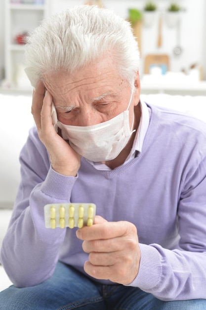 Retrato de un anciano enfermo triste con máscara facial sosteniendo pastillas