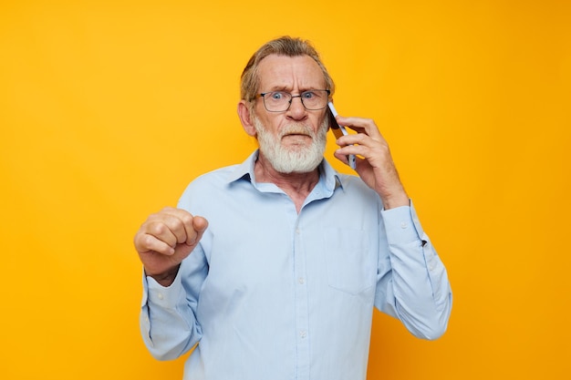 Retrato de un anciano feliz con barba gris y gafas hablando por teléfono con fondo amarillo