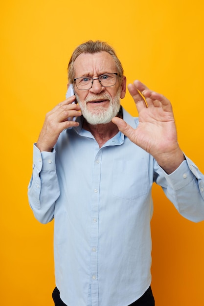 Retrato de un anciano feliz con una camisa azul y gafas hablando por teléfono vista recortada