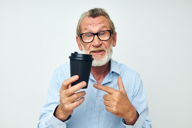 Retrato de un anciano feliz gesticula con sus manos un vaso de bebida de fondo aislado