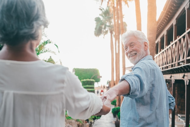 Retrato de un anciano feliz y lindo sosteniendo la mano de la esposa de un jubilado caminando y visitando nuevos lugares junto con la puesta de sol en el fondo Pareja divirtiéndose en el parque