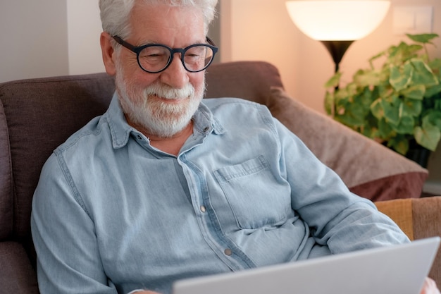 Retrato de un anciano relajado sentado en casa en el sofá usando una computadora portátil navegando por la web