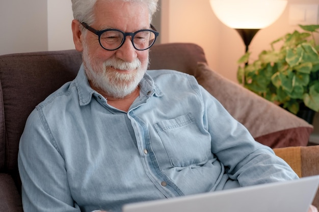 Retrato de un anciano relajado sentado en casa en el sofá usando una computadora portátil navegando por la web