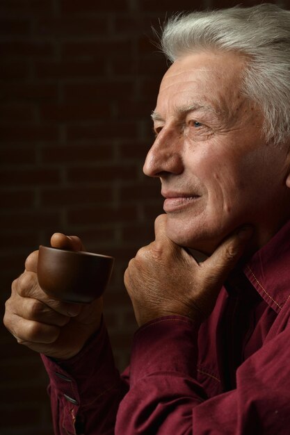 Retrato de un anciano sonriente bebiendo café en casa