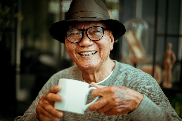 Retrato de un anciano sonriente tomando café mientras está sentado en una cafetería