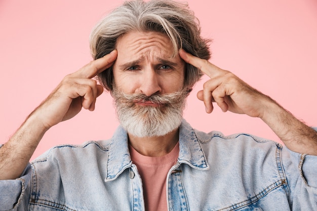 Retrato de anciano tenso con barba gris mirando y tocando sus sienes aislado