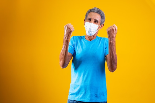 Retrato de ancianos afro con mascarilla quirúrgica celebrando la victoria. ¡Sí!