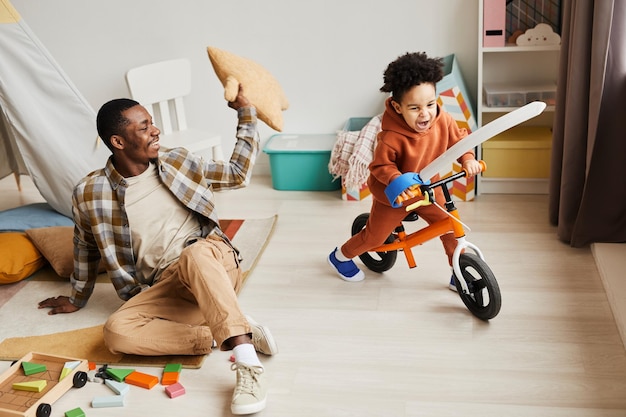 Retrato en ángulo alto de un joven padre despreocupado jugando con su hijo riéndose alegremente en la acogedora habitación de los niños