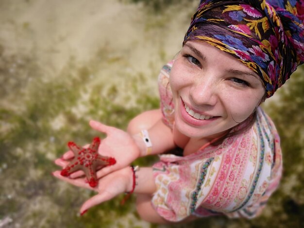 Foto retrato de ángulo alto de una joven sonriente sosteniendo una estrella de mar