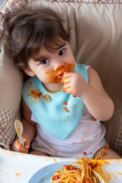 Retrato de ángulo alto de una niña linda, un niño pequeño disfruta comiendo comida con comida sucia alrededor de la boca