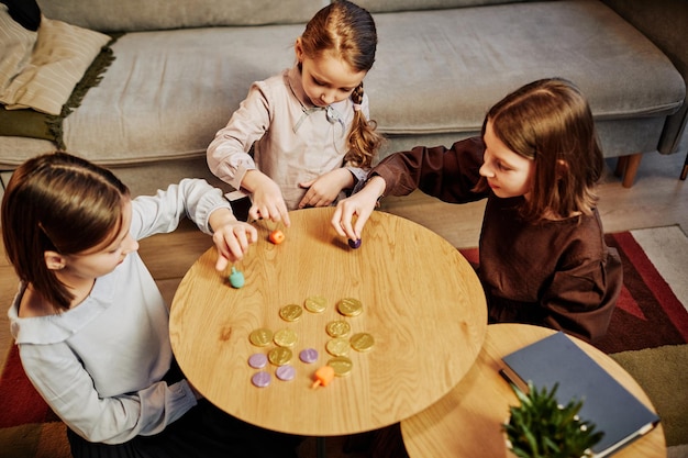 Retrato de ángulo alto de tres niñas jugando al juego de dreidel en un acogedor espacio de copia de ambiente hogareño