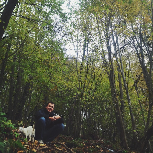 Retrato de bajo ángulo de un hombre sonriente con un gato sentado en el bosque