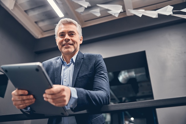 Retrato de ángulo bajo del hombre sonriente con su computadora en la mano en la oficina moderna