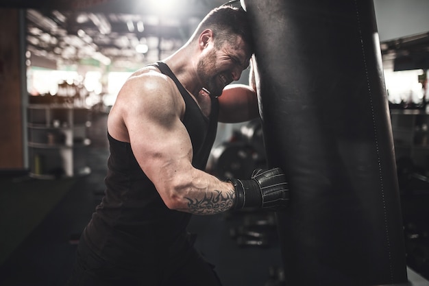 Retrato de ángulo bajo de joven deportista cansado apoyándose en saco de boxeo