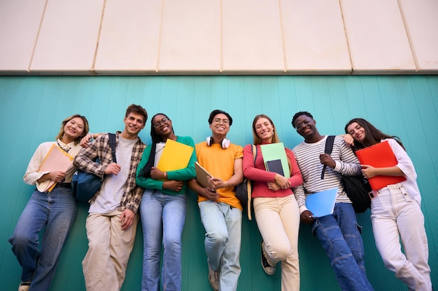 Retrato de ángulo bajo de jóvenes estudiantes multirraciales apoyados contra la pared azul mirando sonriendo a la cámara