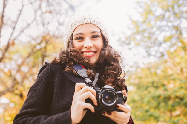 Foto retrato de ángulo bajo de una mujer joven sonriente con ropa cálida mientras sostiene la cámara