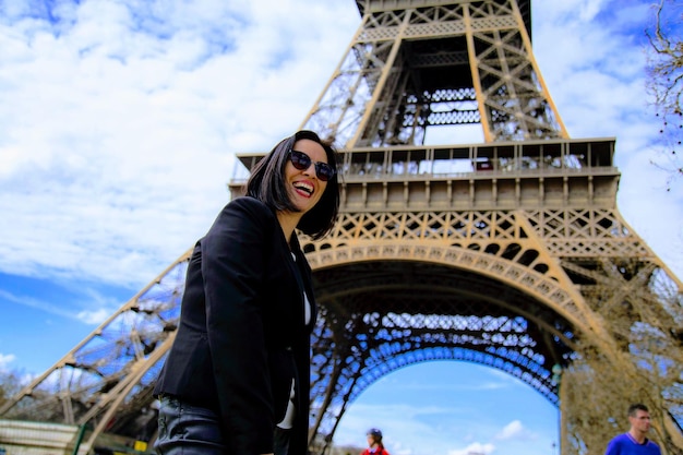 Foto retrato de ángulo bajo de una mujer sonriente de pie contra la torre eiffel