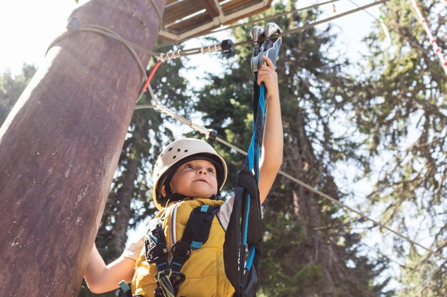 Retrato de ángulo bajo de un niño sosteniendo una cuerda contra los árboles