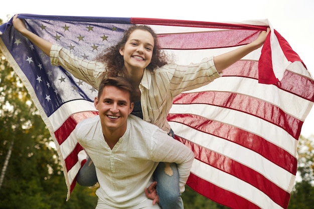 Retrato de ángulo bajo de pareja joven despreocupada ondeando la bandera americana al aire libre