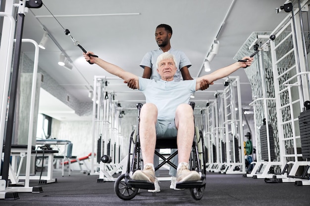 Retrato de ángulo bajo de terapeuta de rehabilitación afroamericano que ayuda a un anciano en silla de ruedas d
