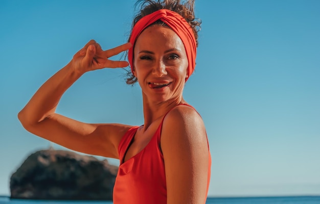 Retrato ao ar livre da bela jovem morena em traje esportivo vermelho com faixa vermelha na praia