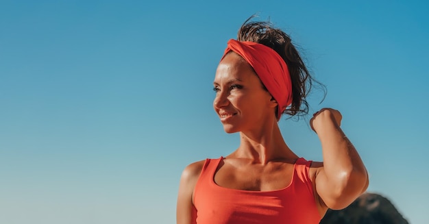 Retrato ao ar livre da bela jovem morena em traje esportivo vermelho com faixa vermelha na praia