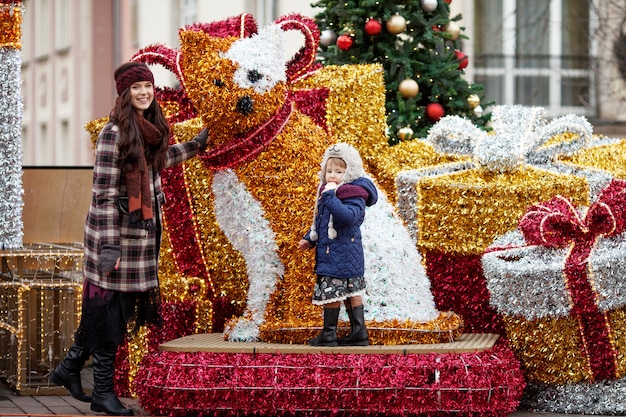 Retrato ao ar livre da mulher sorridente e menina em decorações de Natal na rua da cidade