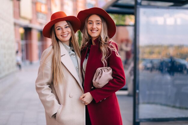 Retrato ao ar livre de duas jovens namoradas lindas em uma rua da cidade usando um elegante chapéu de casaco